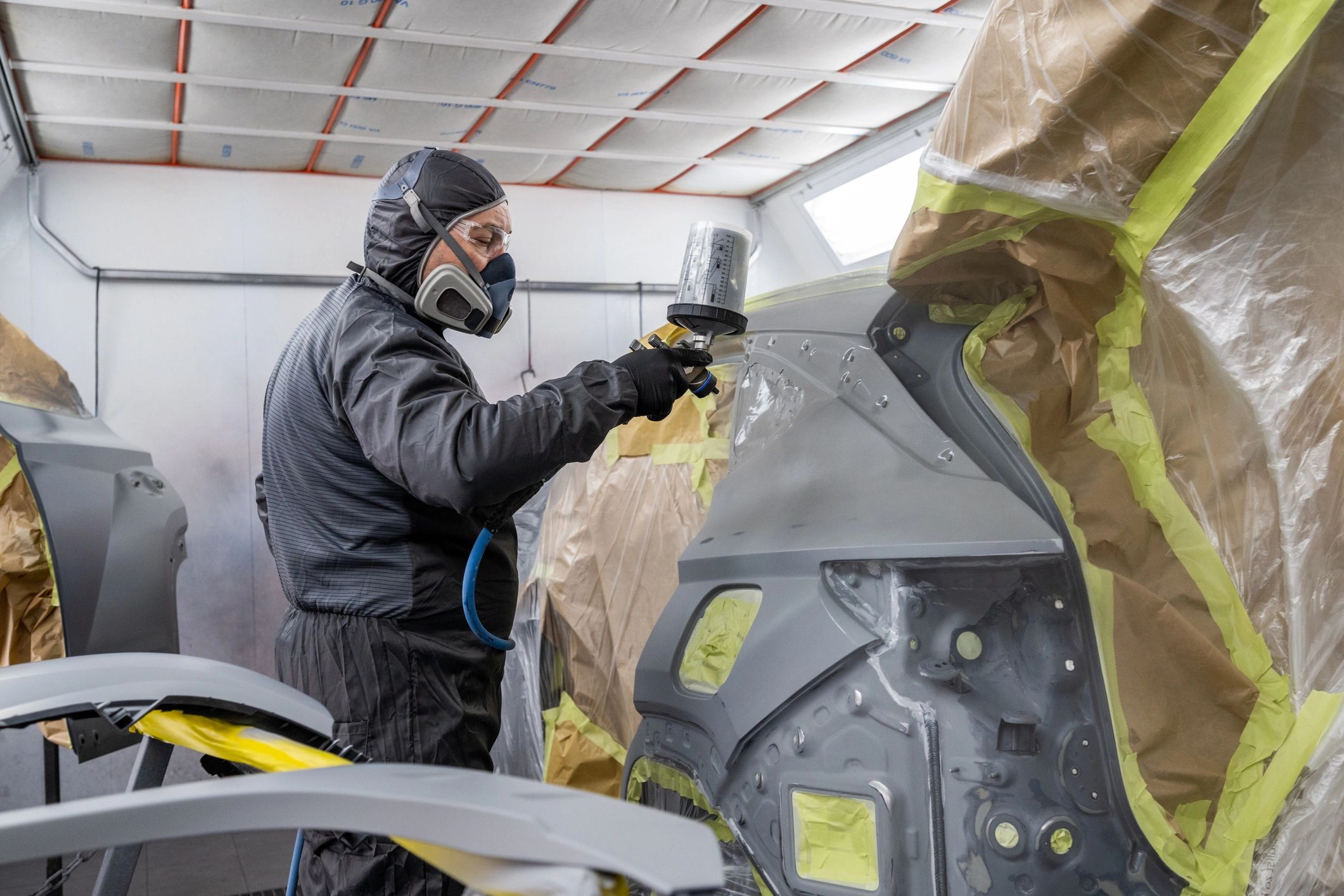 Automotive painter applying spray coat to a car panel in a paint booth